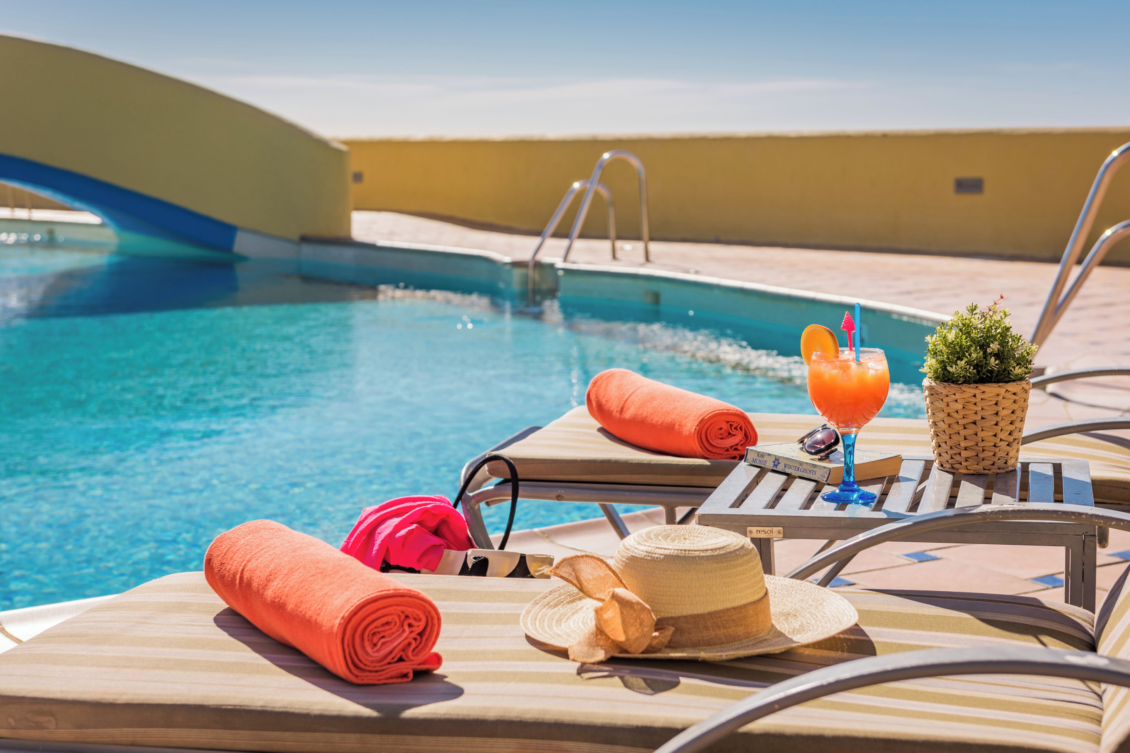 Un espace de détente aménagé au bord de la piscine, avec des chaises longues, une piscine et un petit pont.