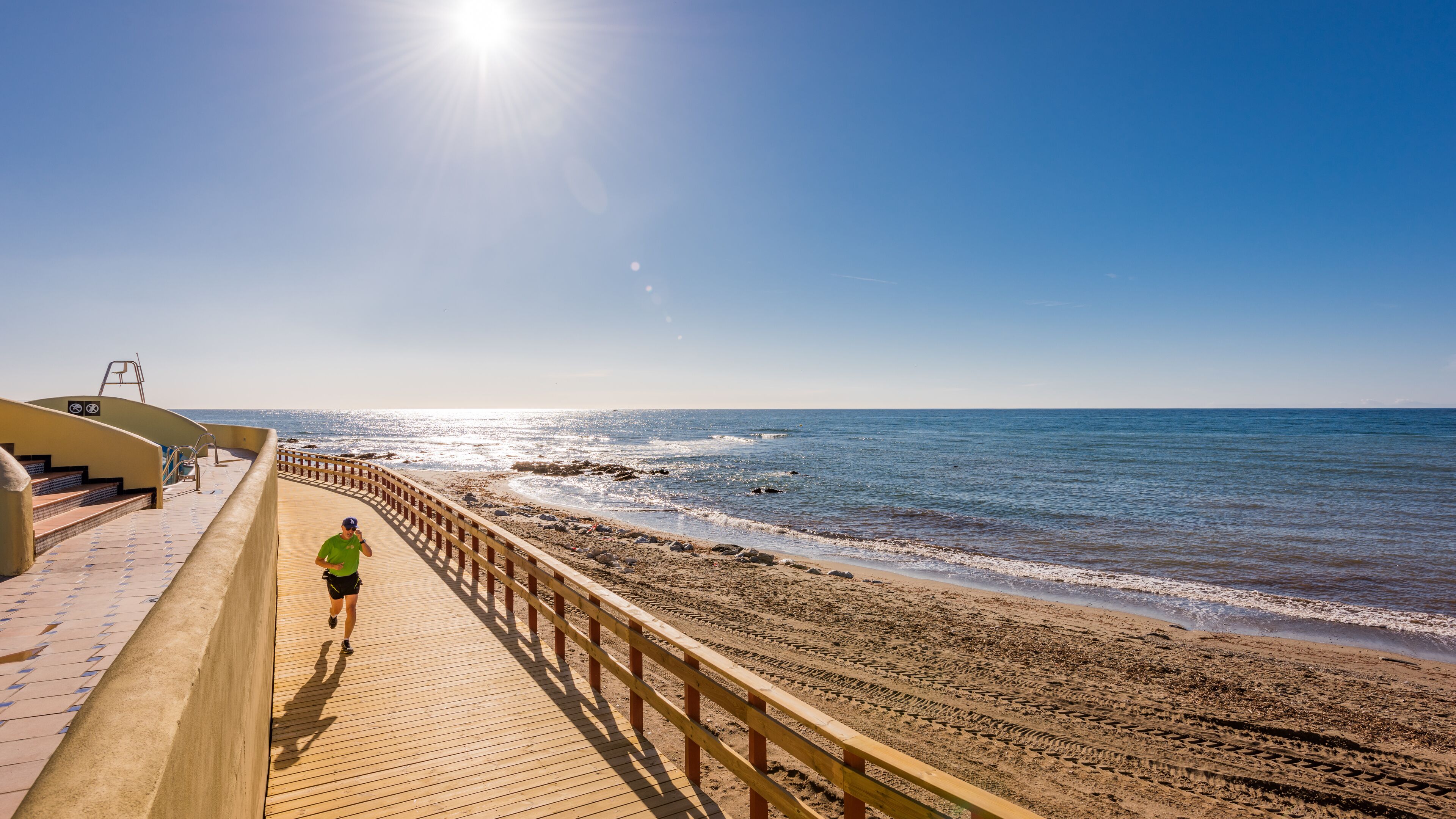 Un muelle de madera que conduce a una playa, con cielo despejado y sol brillante.