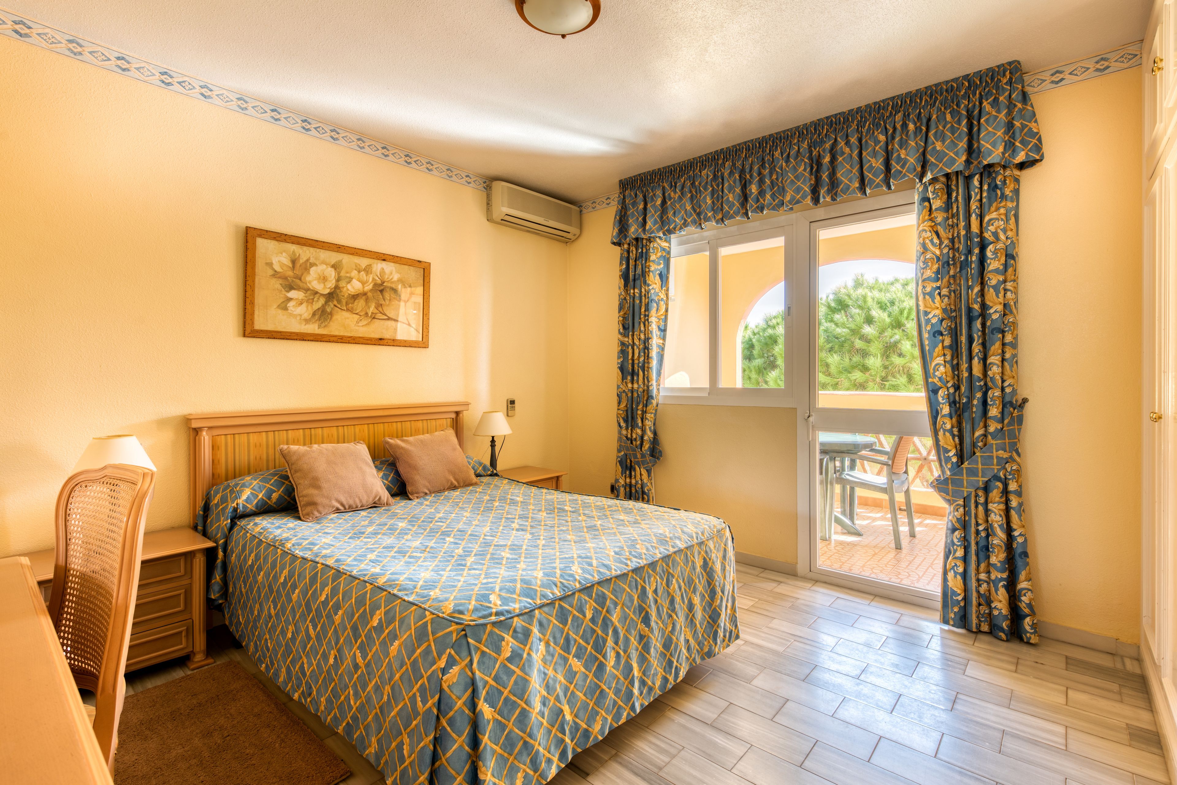 A bedroom with a bed, a nightstand, a chair, a window with curtains, and a view of the outdoors.