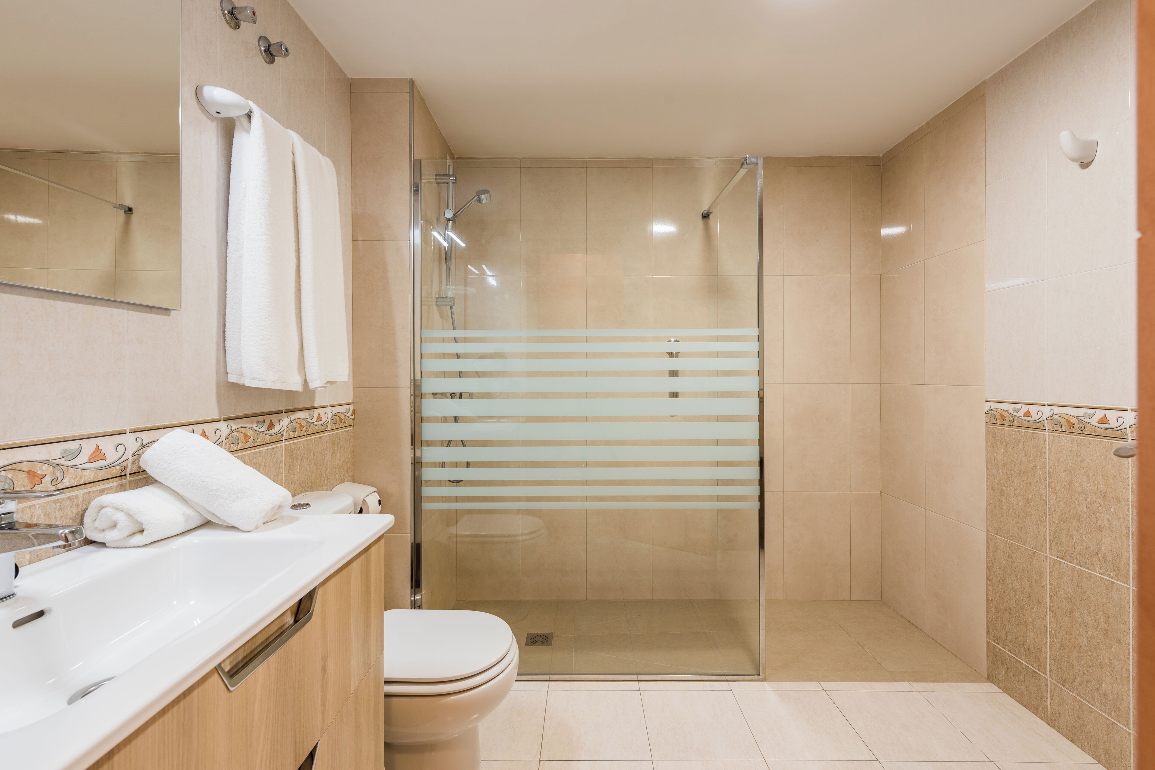 Une salle de bain moderne dotée d’une douche à parois de verre, de toilettes et d’un meuble-lavabo avec un miroir et un porte-serviettes.