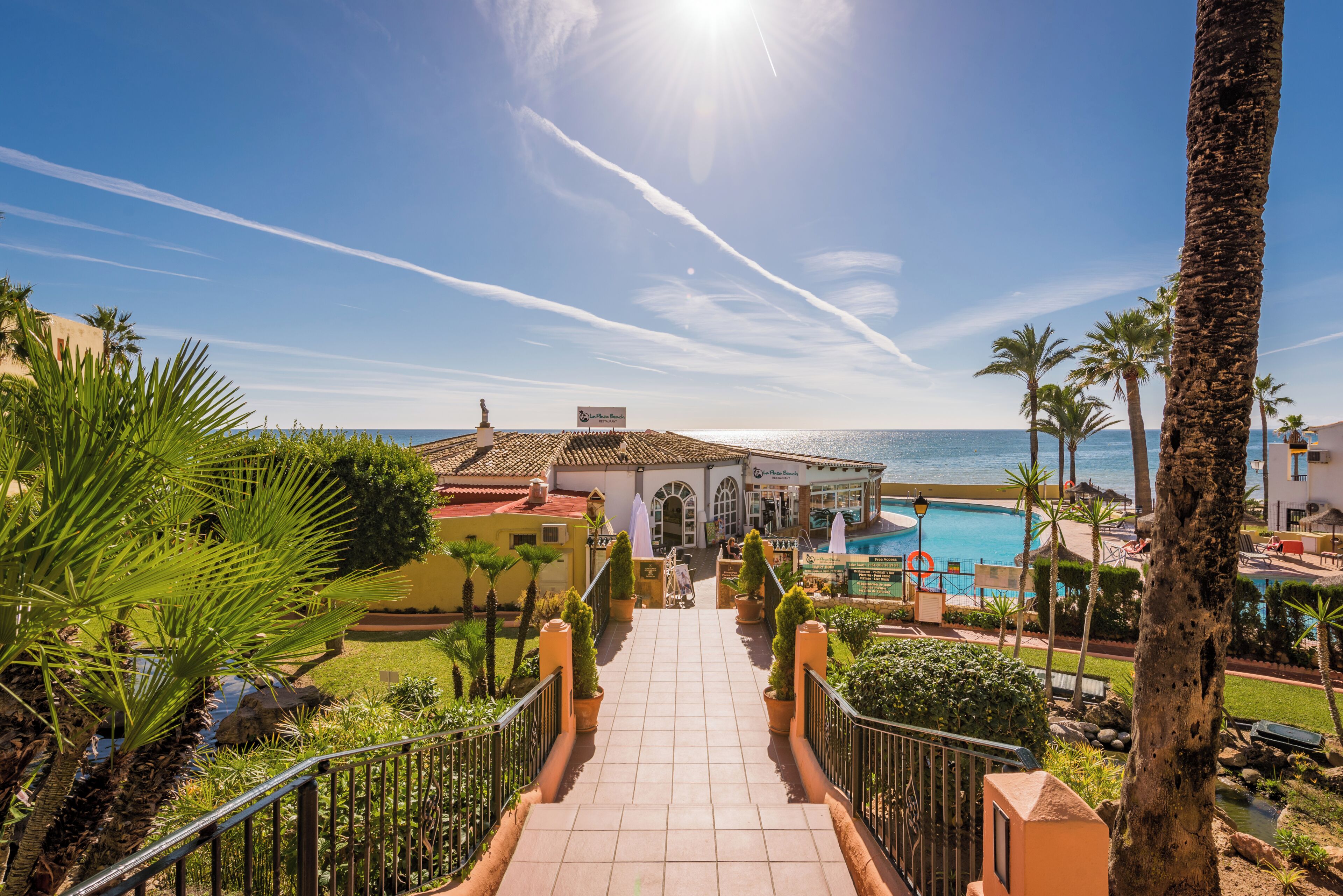 Un resort con piscina, palmeras y una vista despejada del mar.