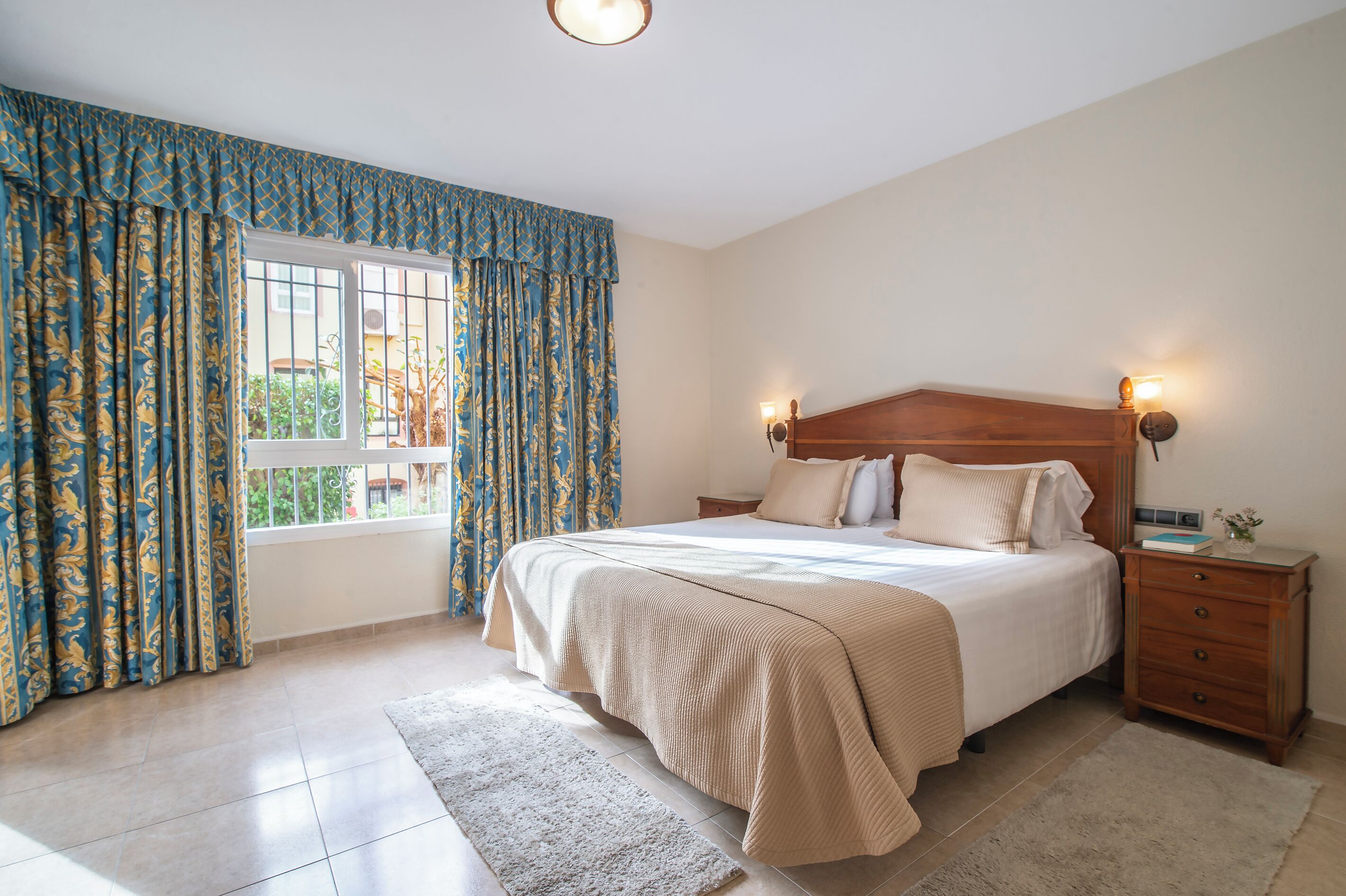 Een slaapkamer met een groot bed, twee nachtkastjes, een venster met gordijnen.