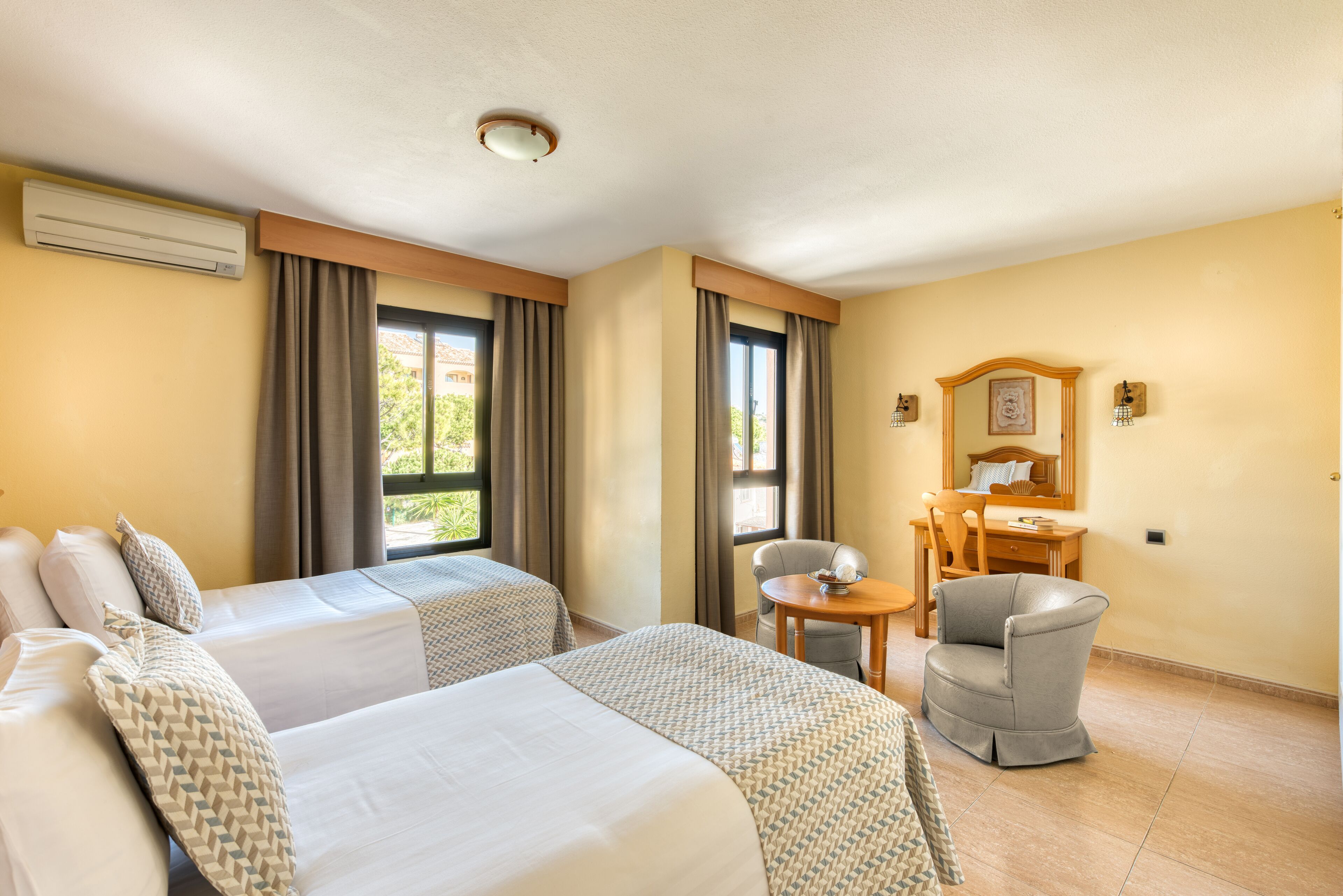 A hotel room with two beds, a desk, a chair, and a window with curtains.