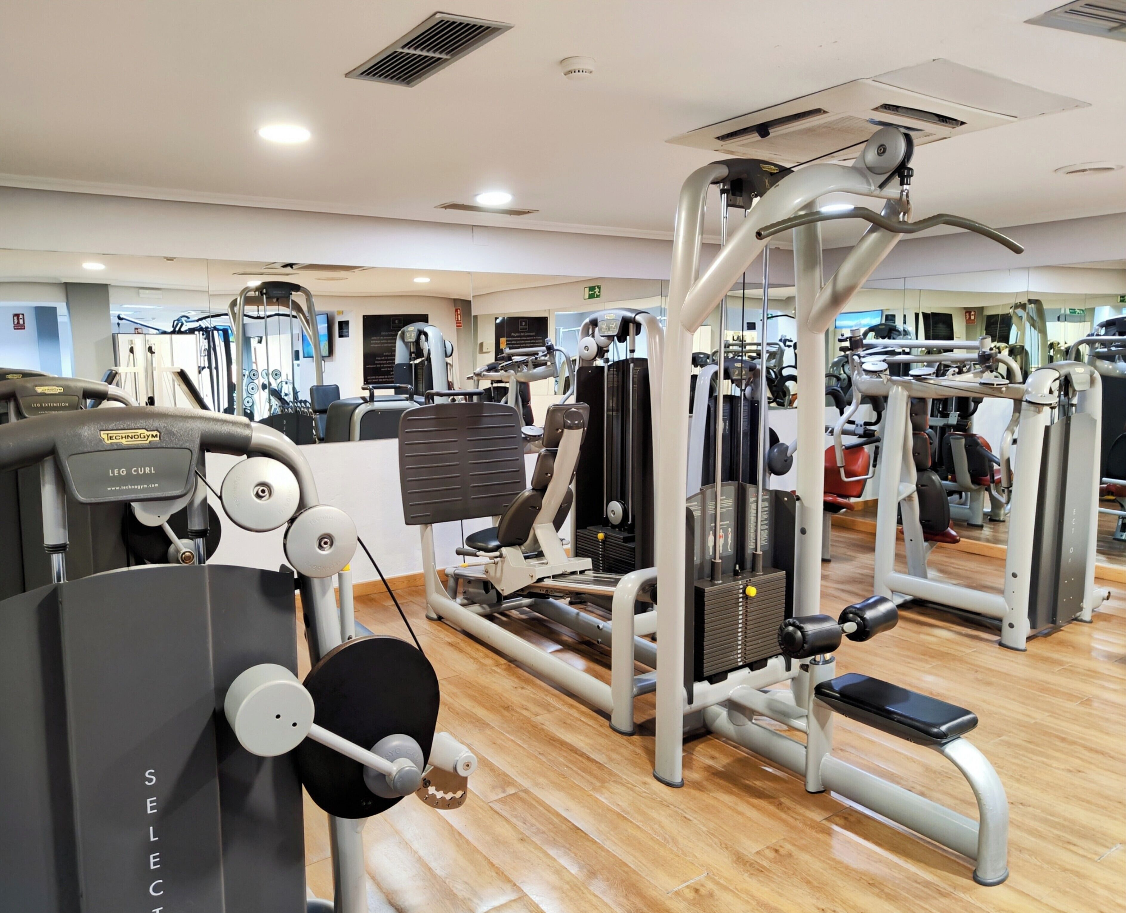 A gym with various exercise machines, mirrors, and a wooden floor.