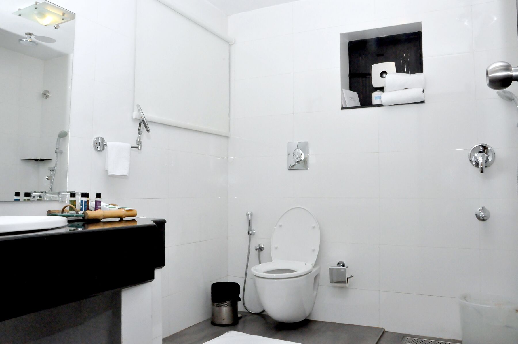 A modern bathroom with a white tiled wall, a toilet, a shower, and a sink with a black countertop.