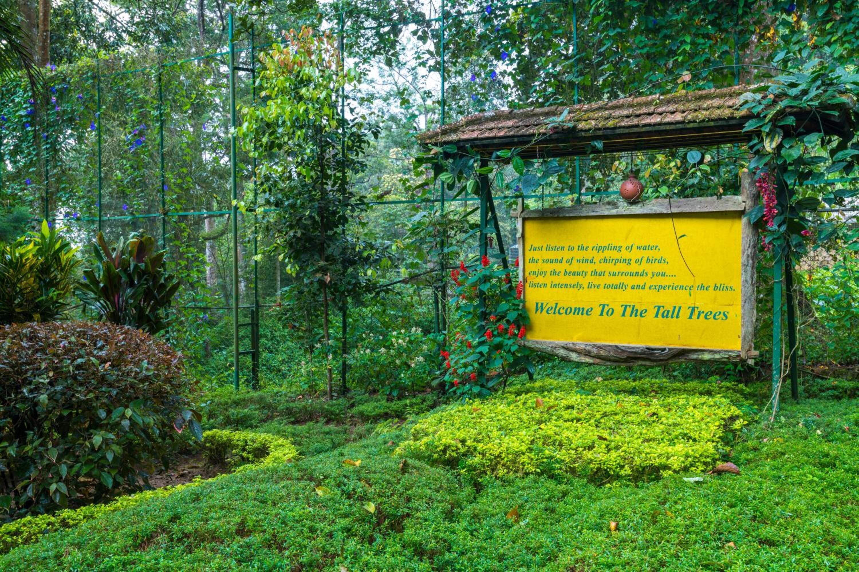 A sign welcoming visitors to a lush garden with a pergola structure.