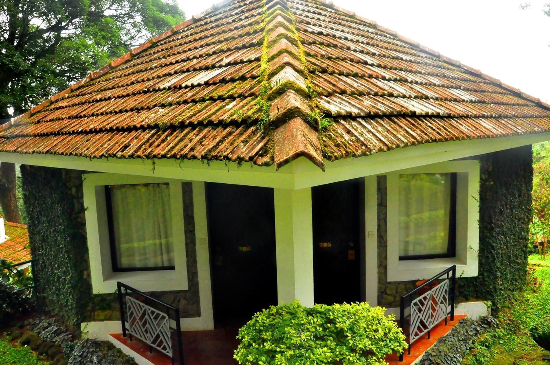 A small, single-story structure with a tiled roof, two windows with white frames, and a small porch with a railing.