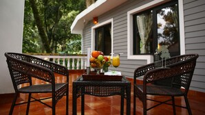 Un patio con sillas de mimbre, una mesa con frutas y bebidas, y una casa con ventana y barandilla.
