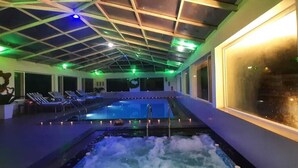 Una piscina interior con sillas de descanso y un jacuzzi, bajo un techo de cristal con iluminación verde.
