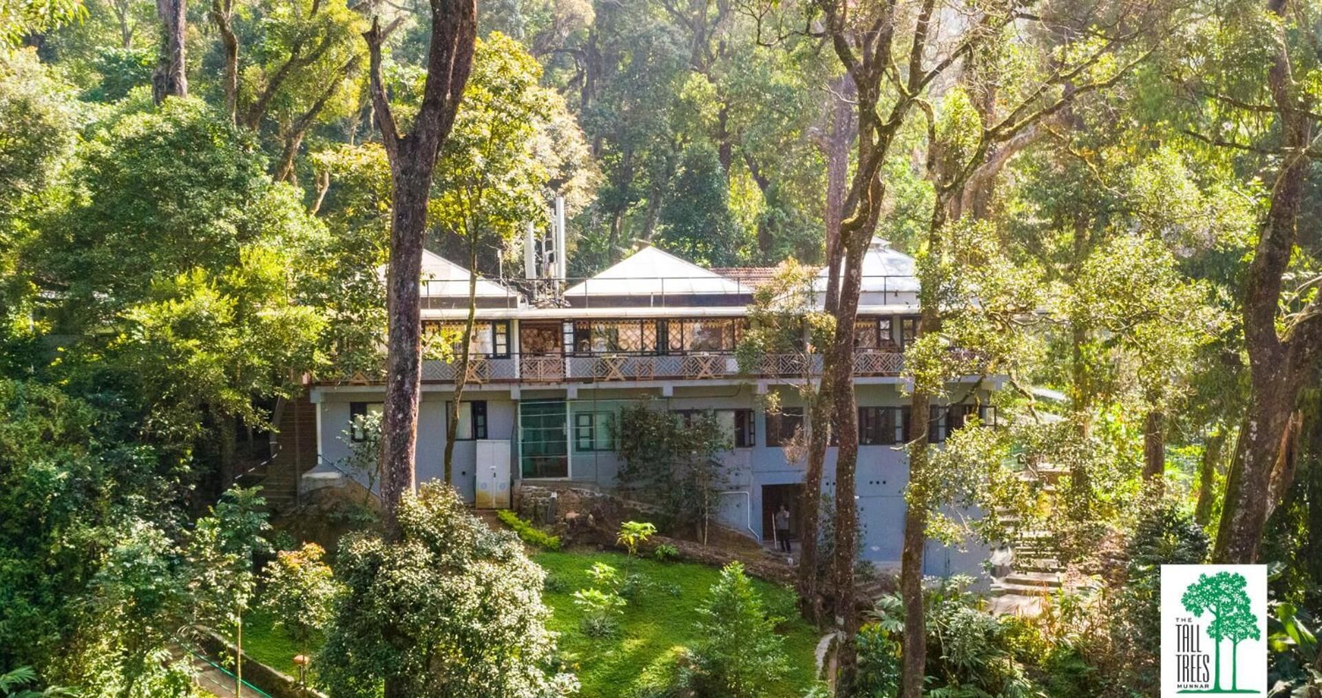 Une maison à deux étages entourée d’une forêt dense.