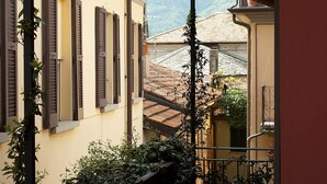A narrow alleyway with buildings on either side, featuring shutters and a view of a mountain in the background.