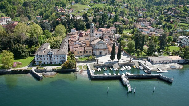 An aerial view of a historic town with a prominent church, a marina with boats, and lush greenery.