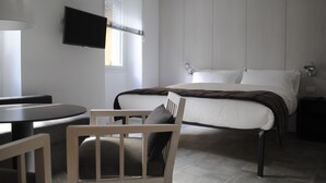A modern hotel room with a bed, a desk, a chair, and a TV mounted on the wall.