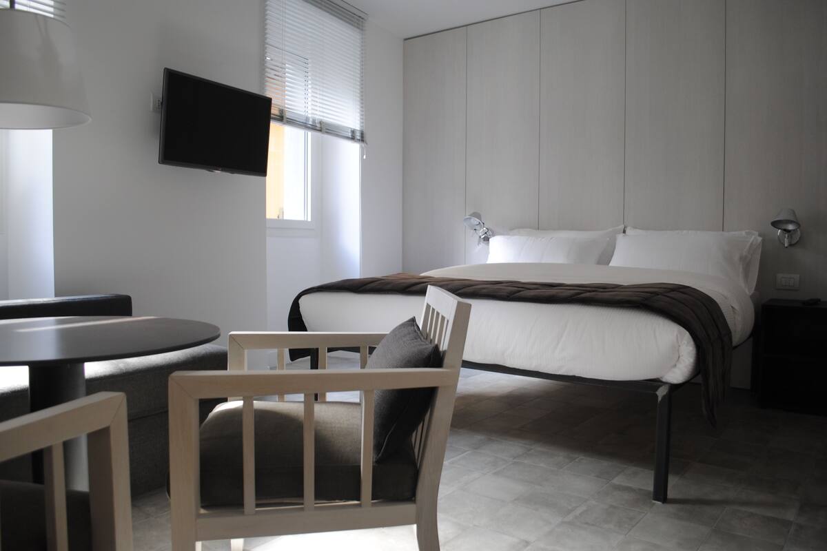 Una habitación de hotel moderna con una cama, un escritorio, una silla y un televisor montado en la pared.