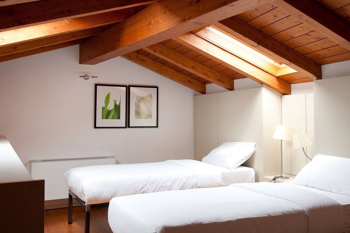 Una habitación con dos camas, vigas de madera, un tragaluz y dos cuadros enmarcados en la pared.