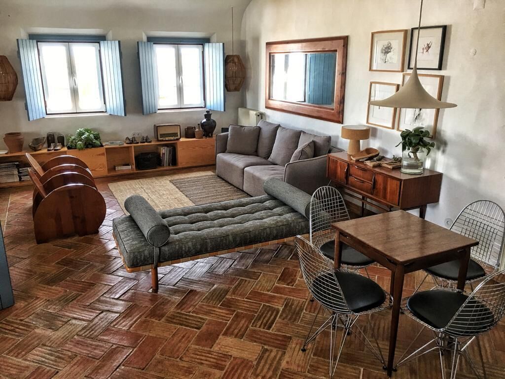 Una sala de estar acogedora con un sofá, una mesa de comedor y sillas. Hay ventanas con cortinas azules, piso de madera y un espejo grande en la pared.