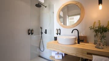 Une salle de bain moderne avec une douche à parois de verre, un miroir rond, un meuble-lavabo en bois et un vase rempli de fleurs jaunes.