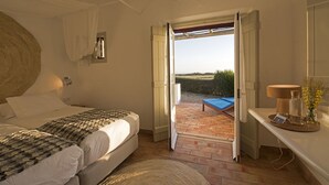 A bedroom with a bed, bedside table, and a view of the outdoors. - Herdade Do Touril (Odemira)