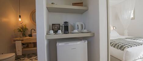 A compact hotel room with a kitchenette, a bed with a canopy, a small refrigerator, and a bathroom with a toilet and sink.
