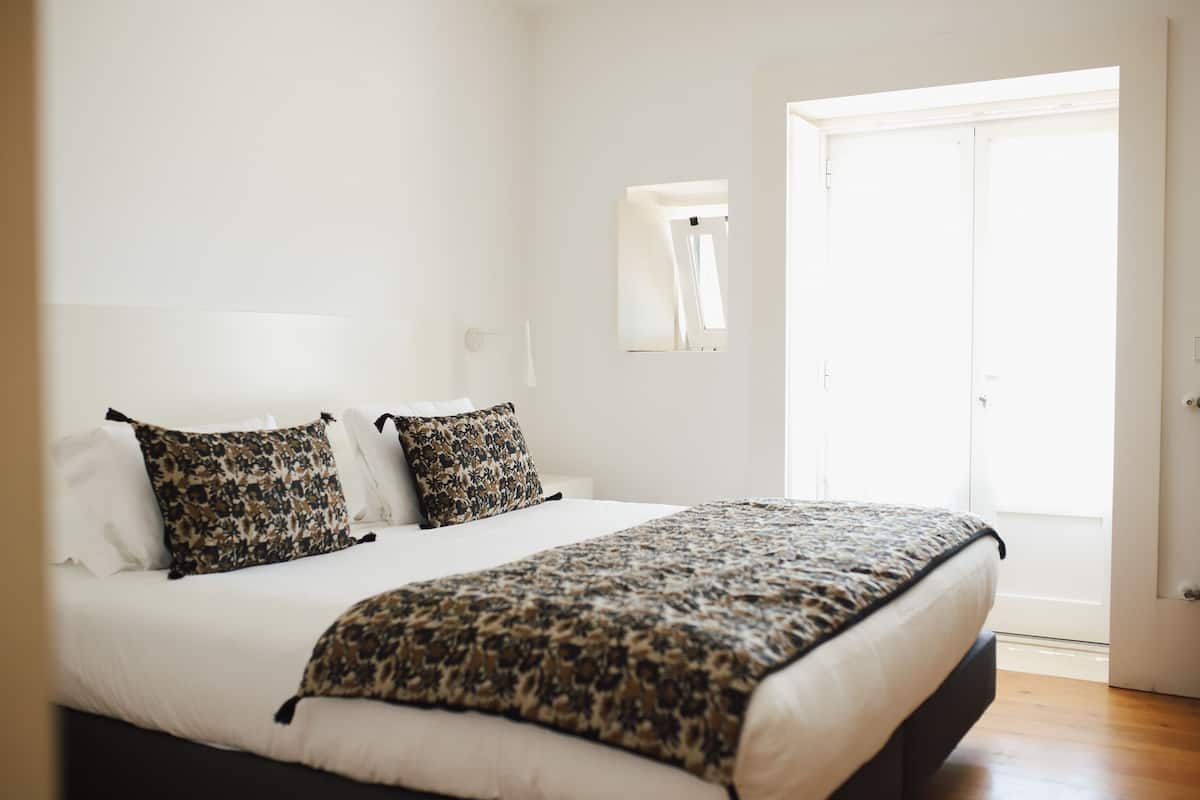 A bedroom with a bed, two pillows, a bedside table, and a window.
