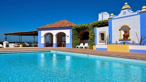A poolside area with a clear blue pool, a building with a tiled roof, and a blue and yellow facade. - Herdade Do Touril (Odemira)