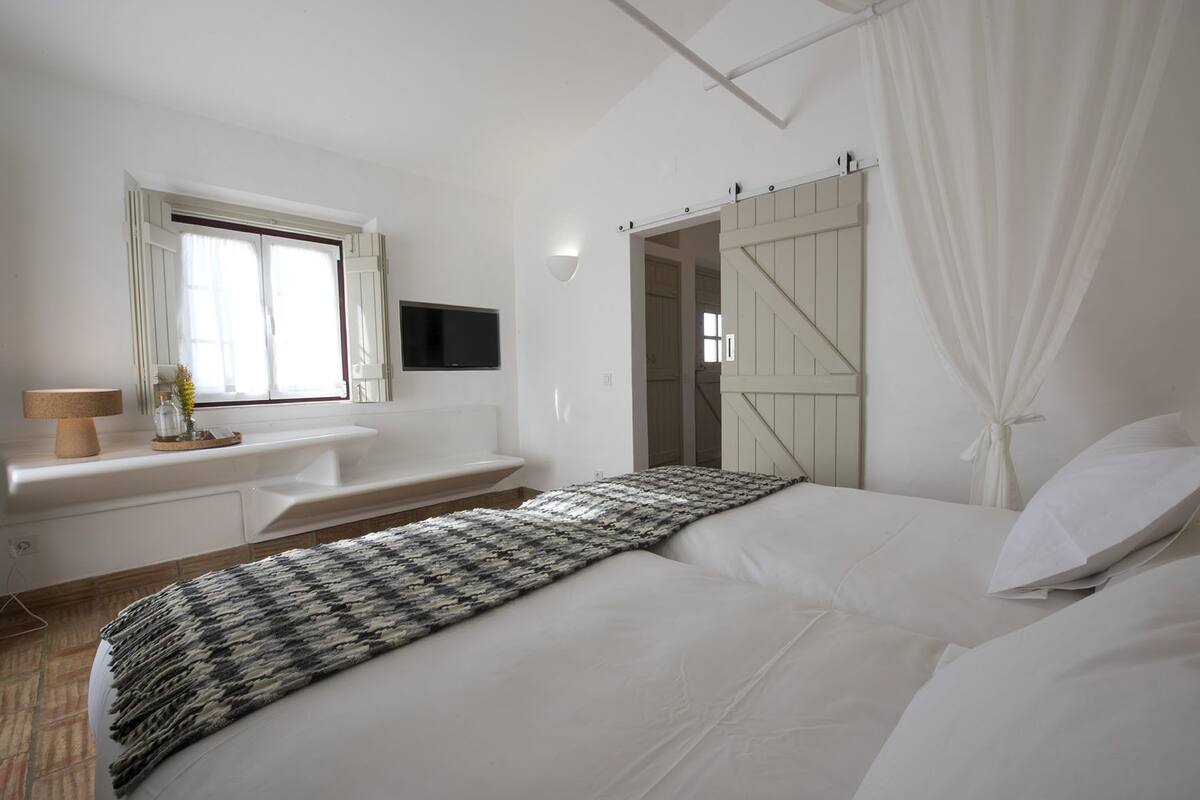 A bedroom with a bed, a bedside table, a TV, a window, and a sliding door.