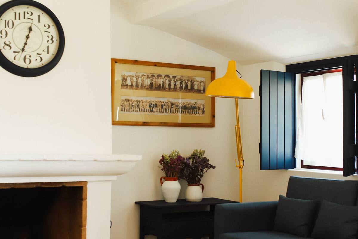 A living room with a fireplace, a clock, a sofa, a table, and a lamp.