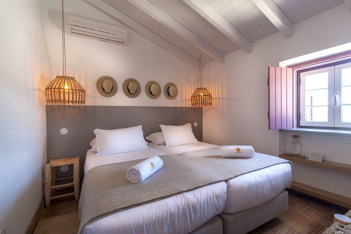 A double bed with white linens, a wooden ladder, and a small bedside table.