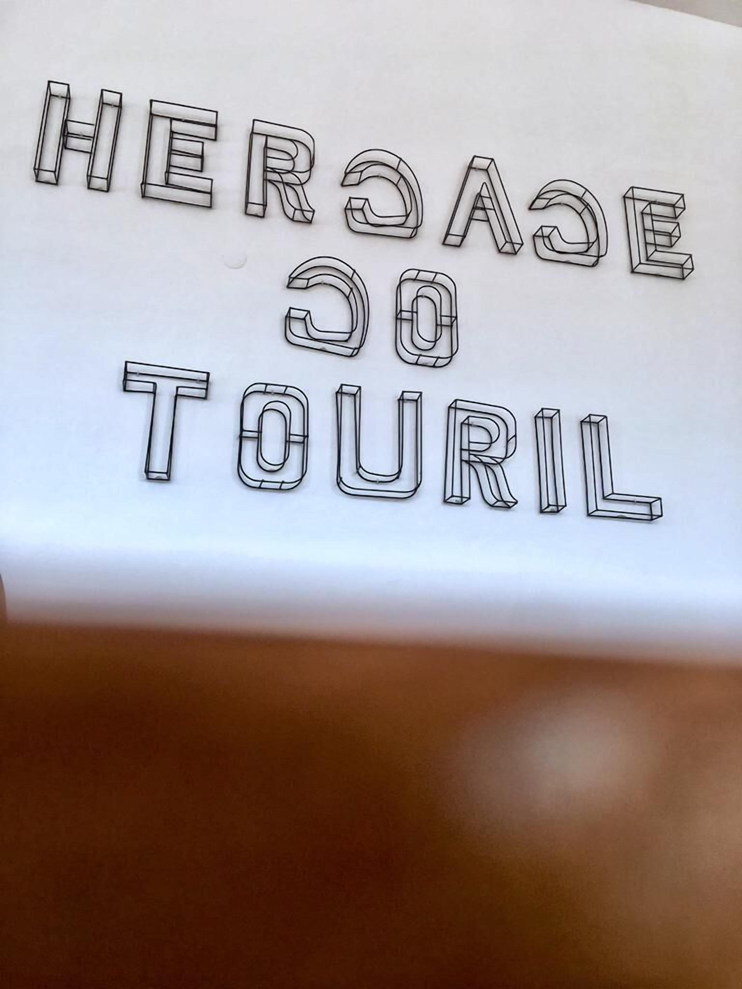 A sign with the text "HERSAJE GO TOURIL" in a stylized font.