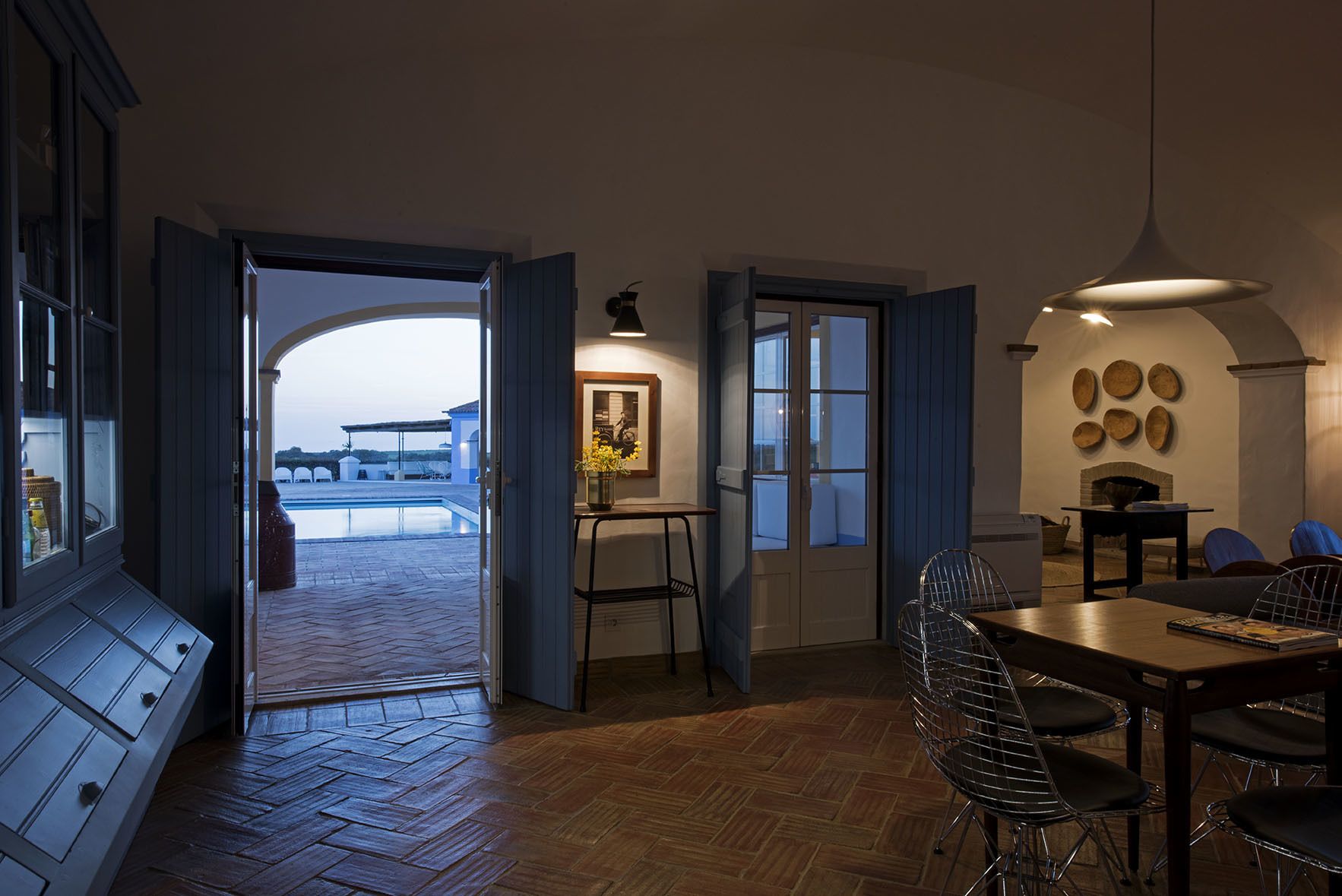 A dining area with a wooden table and chairs, a hanging light fixture, and a view of an outdoor swimming pool.