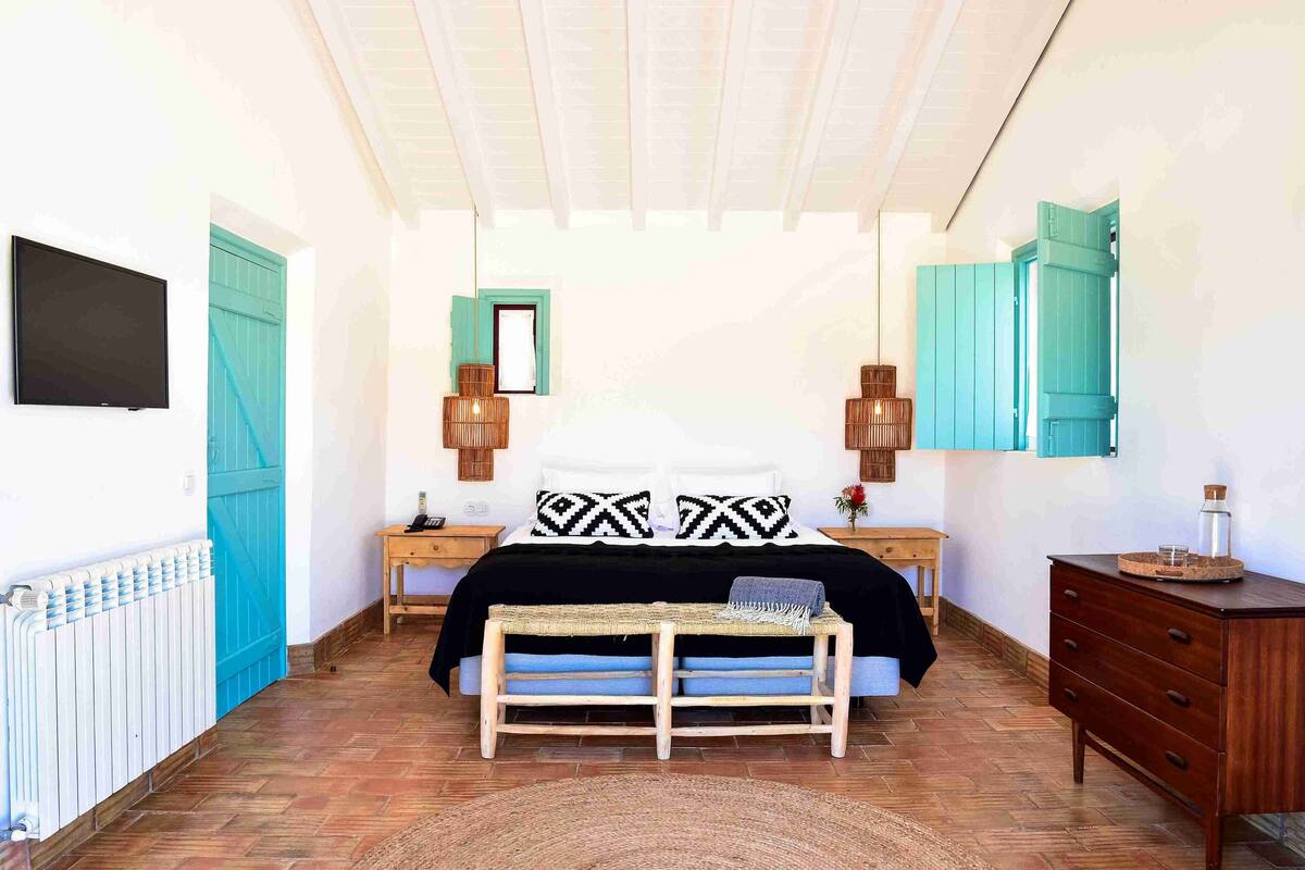 A bedroom with a bed, bedside tables, a bench, a dresser, and a TV on the wall.