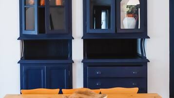 A dining area with a wooden table and chairs, a dark blue cabinet with glass doors, and a white air conditioning unit on the wall.