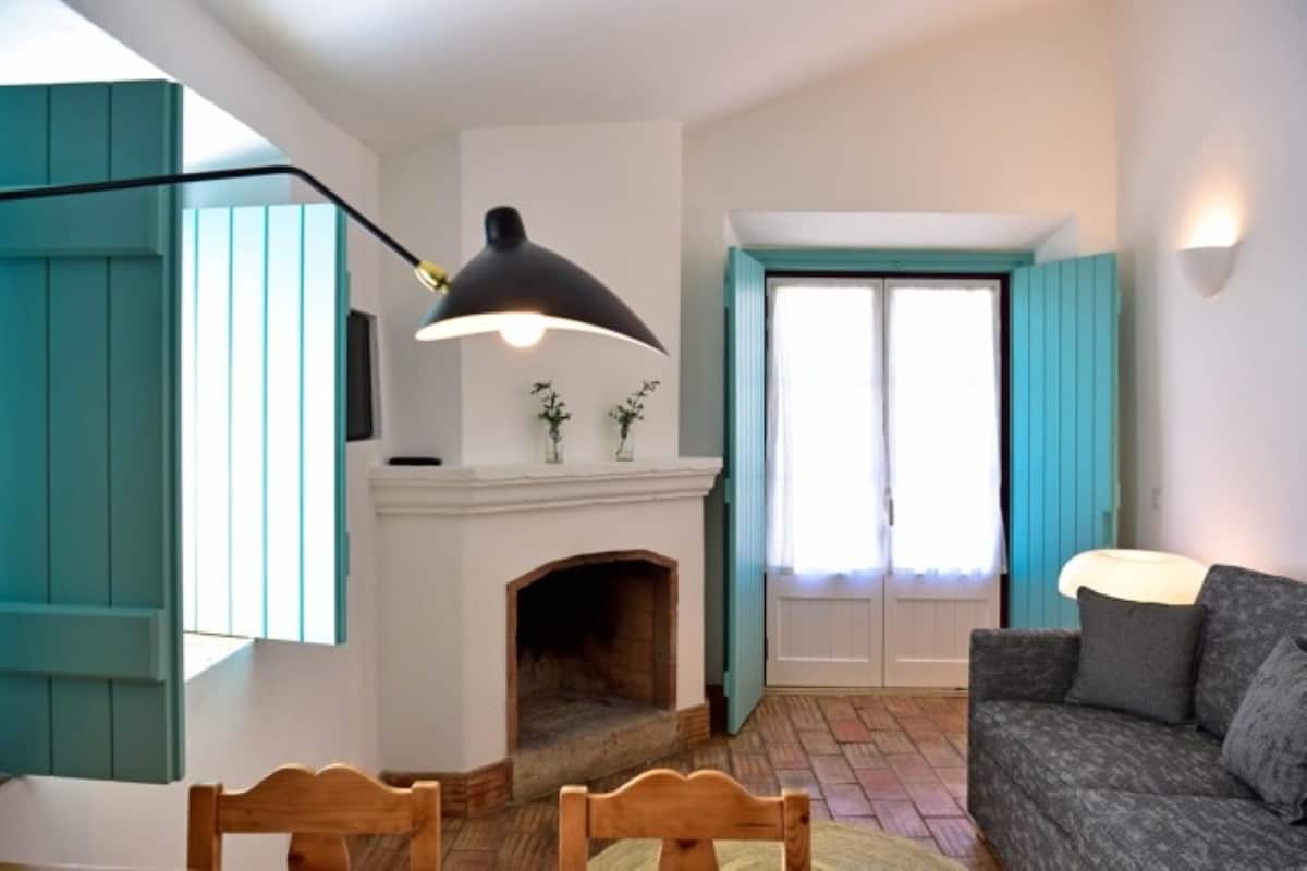 A cozy living room with a fireplace, teal accents, a sofa, and a table with chairs.