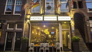 A hotel with a restaurant and lounge area, featuring a brick facade, multiple flags, and outdoor seating with chairs and tables.