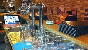 A bar area with multiple taps, a stack of glasses, and a digital screen displaying images.