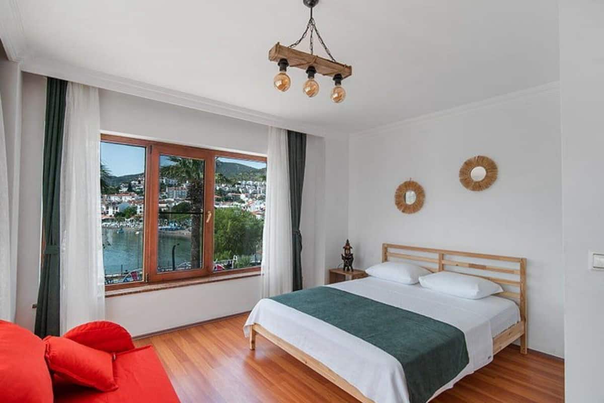 Une chambre avec un lit en bois, une vue sur la ville par une grande fenêtre et un canapé rouge.