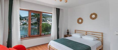 A bedroom with a wooden bed, a view of a town through a large window, and a red sofa.