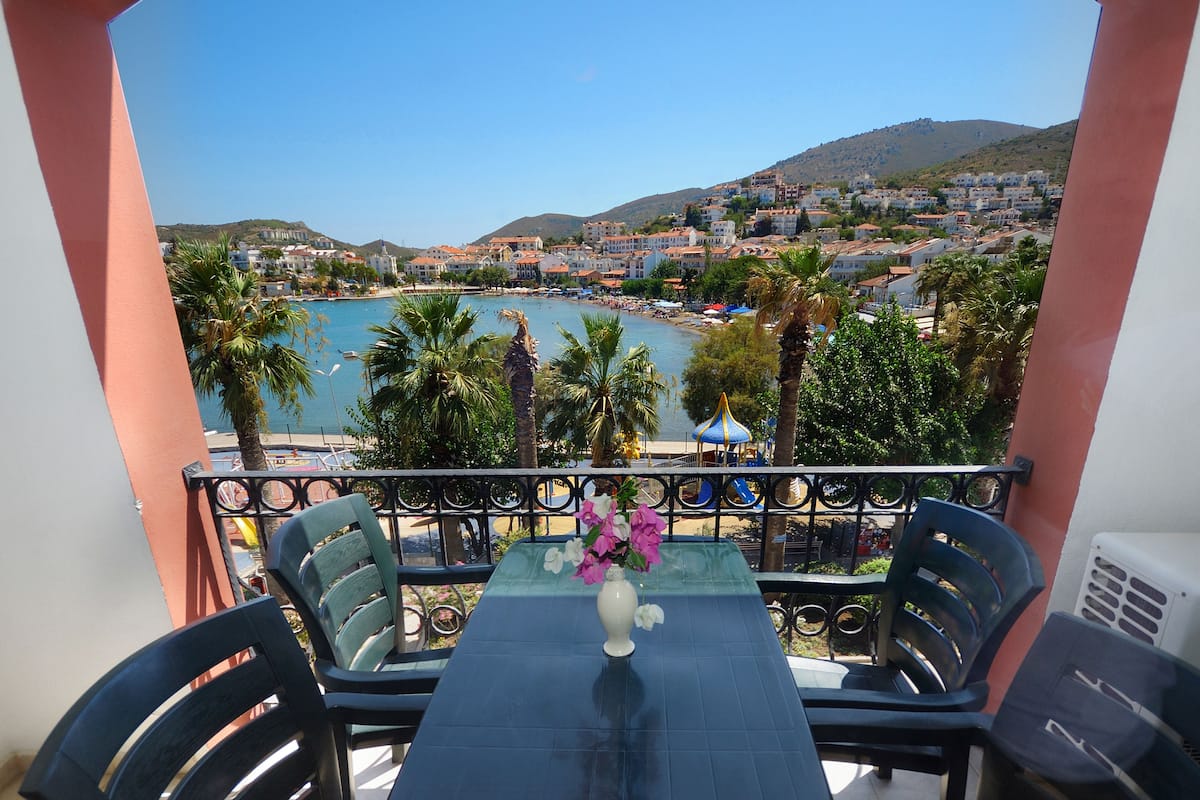 Un balcon avec une table et des chaises, donnant sur une ville côtière avec une plage et des collines.