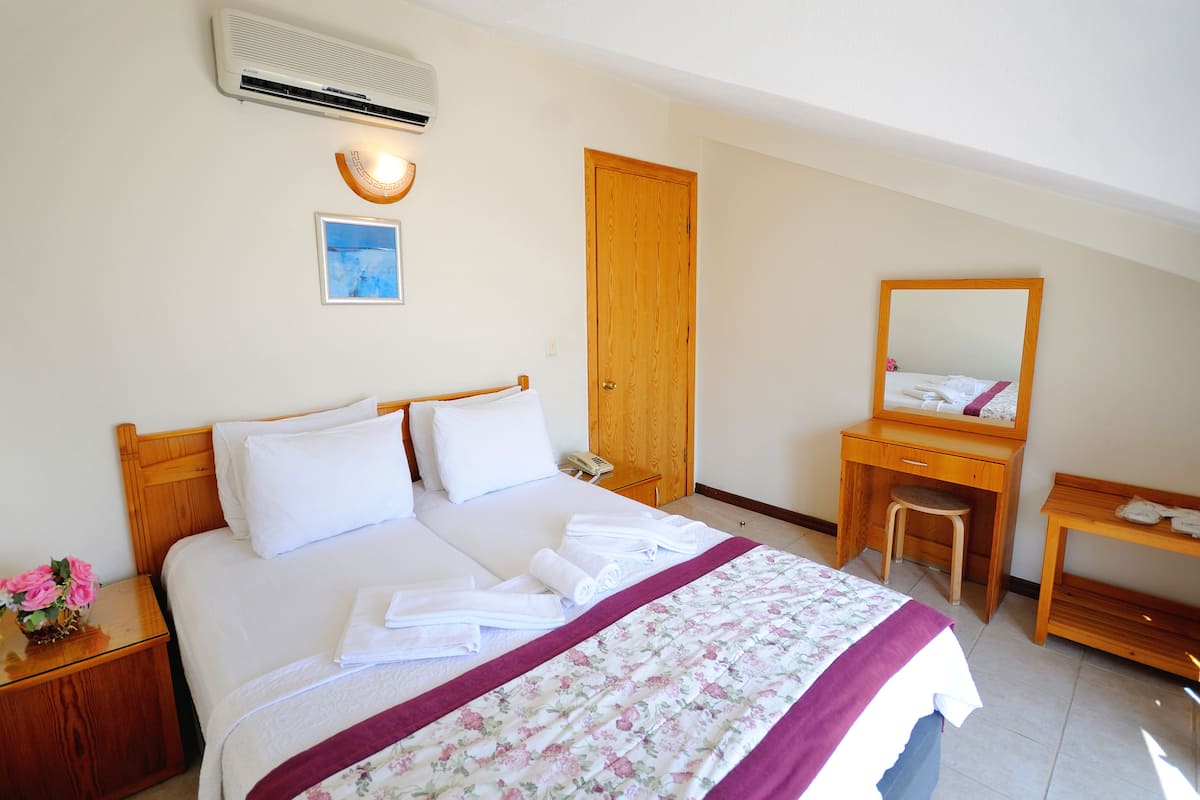 Une chambre d’hôtel bien aménagée, avec un lit, une table de chevet, un bureau en bois, une chaise, un miroir et un climatiseur fixé au mur.