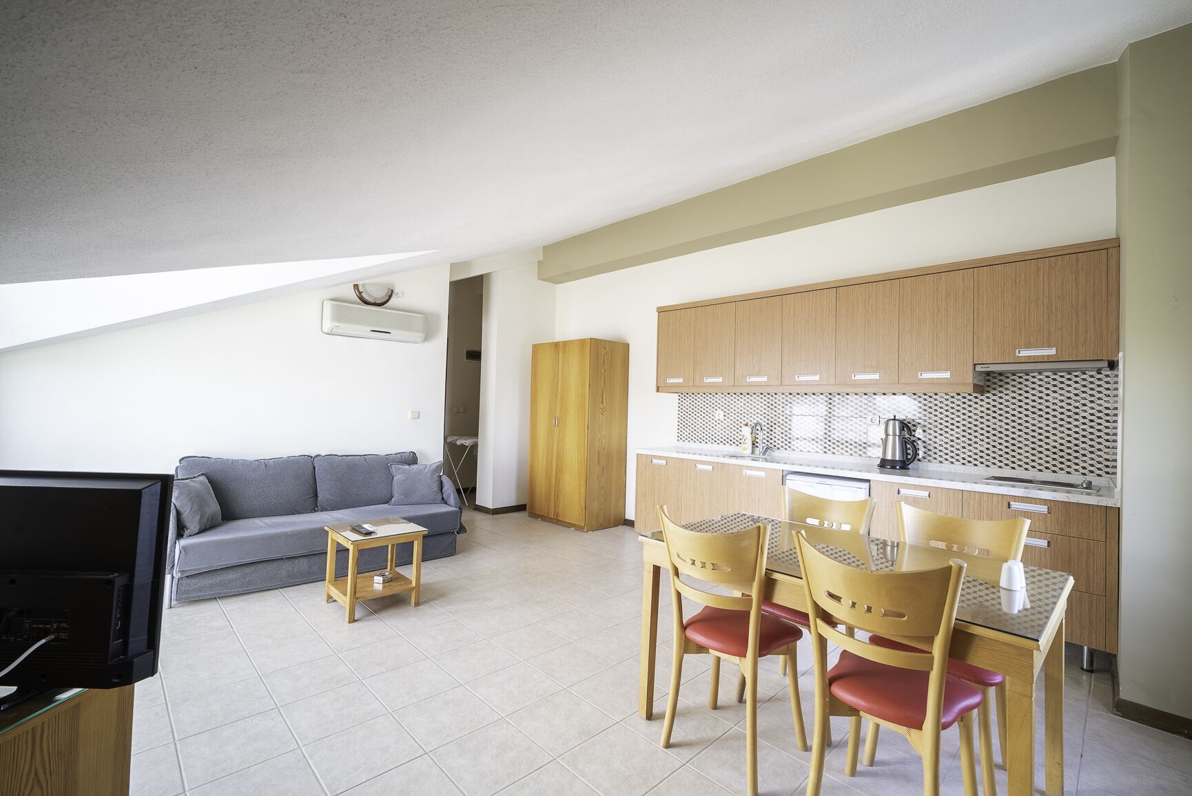 A compact living space with a kitchenette, a sofa, a small table, and a dining area with chairs.