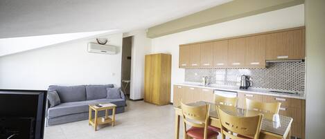 A compact living space with a kitchenette, a sofa, a small table, and a dining area with chairs.