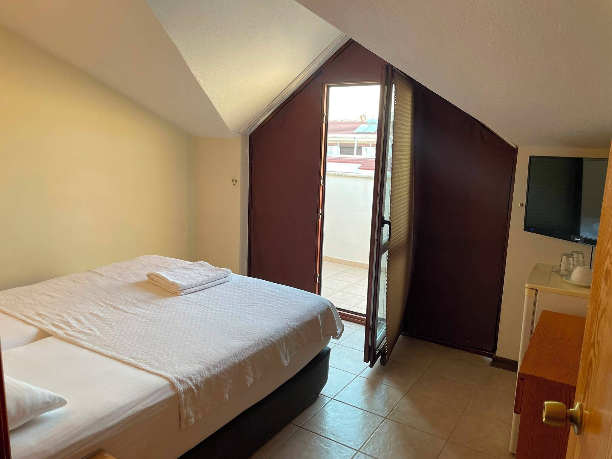 A hotel room with a bed, a television, a door, and a window.