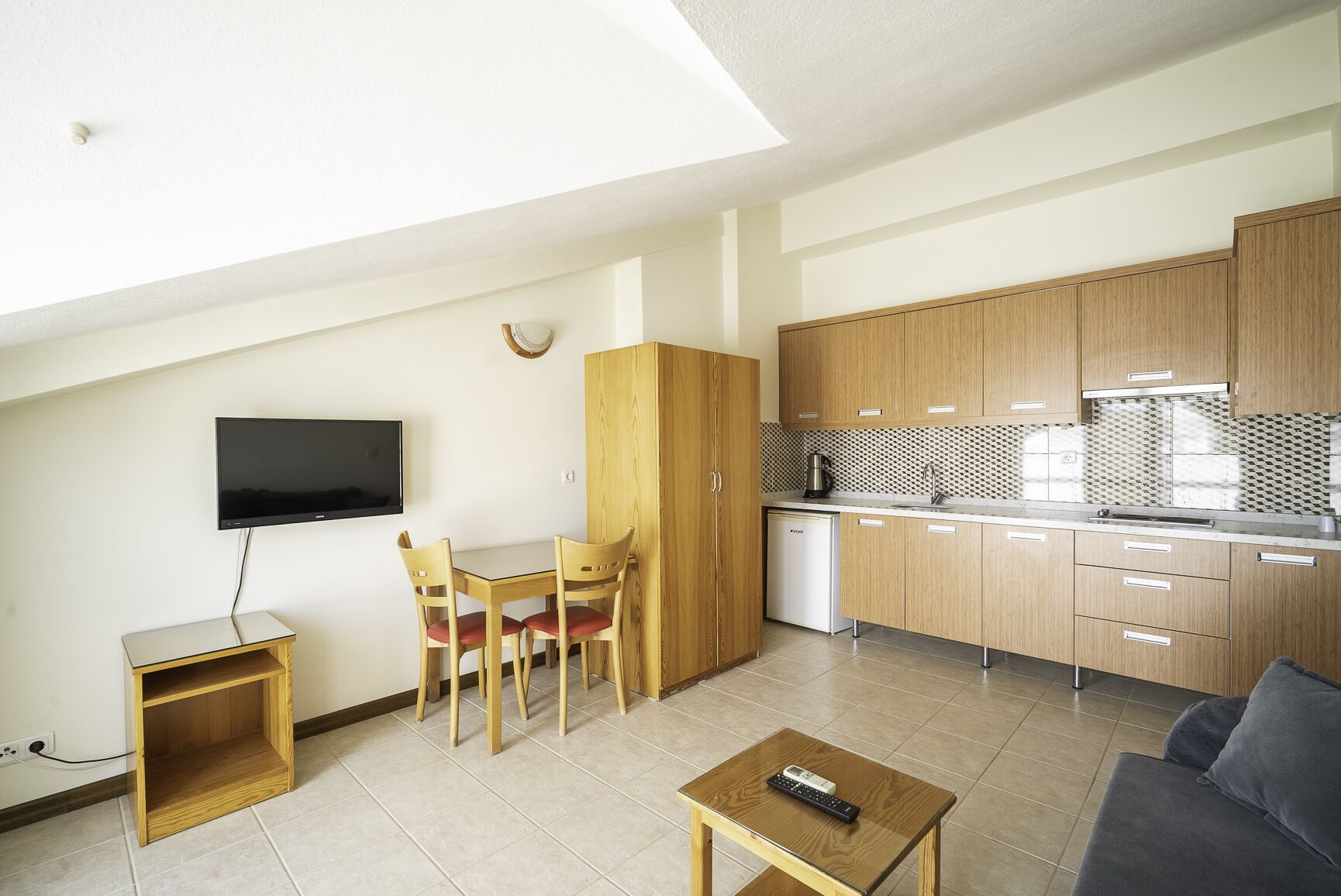 A compact living space with a dining area, kitchenette, and a TV mounted on the wall.