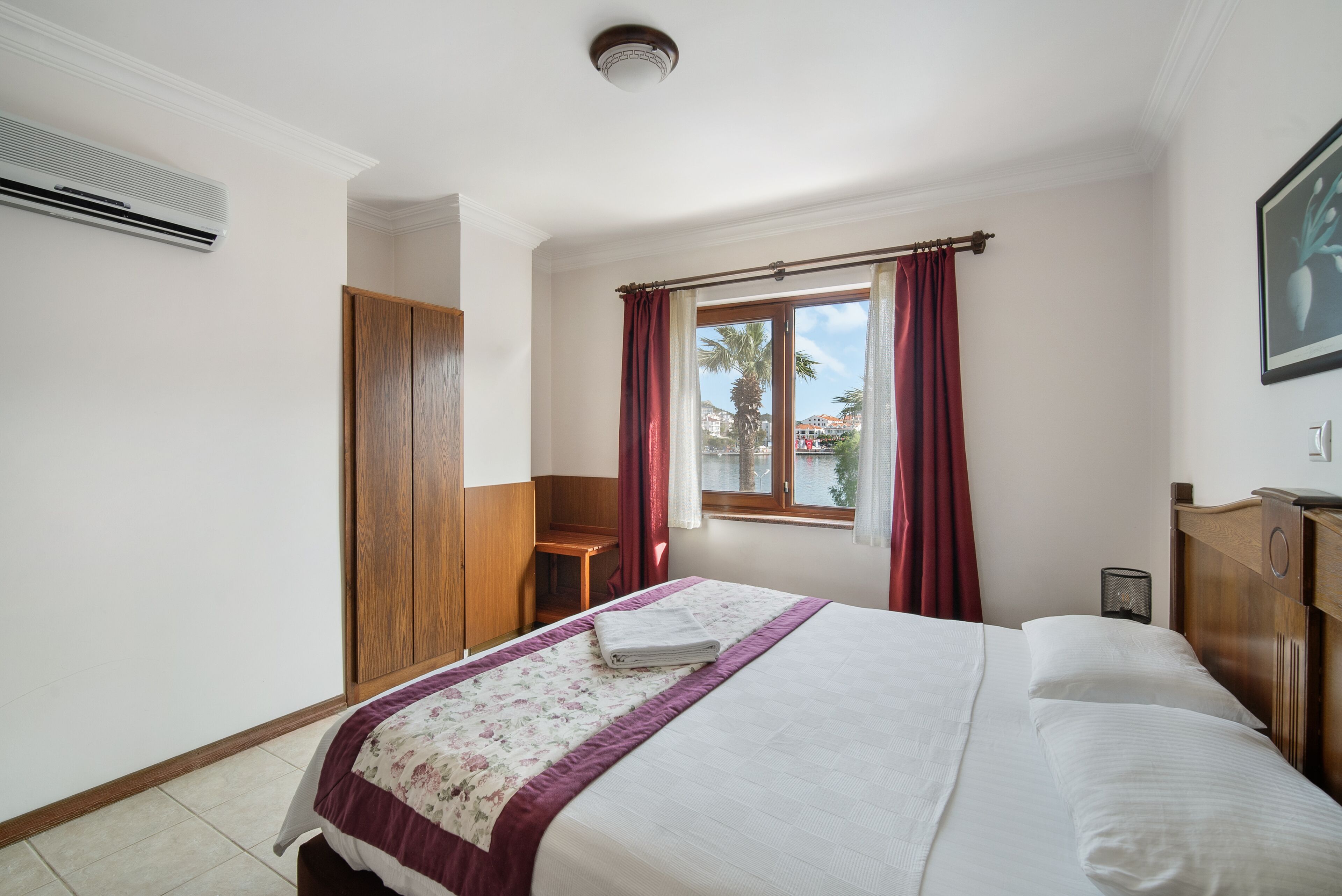 A neatly arranged bedroom with a bed, a wooden wardrobe, a desk, and a window with curtains.