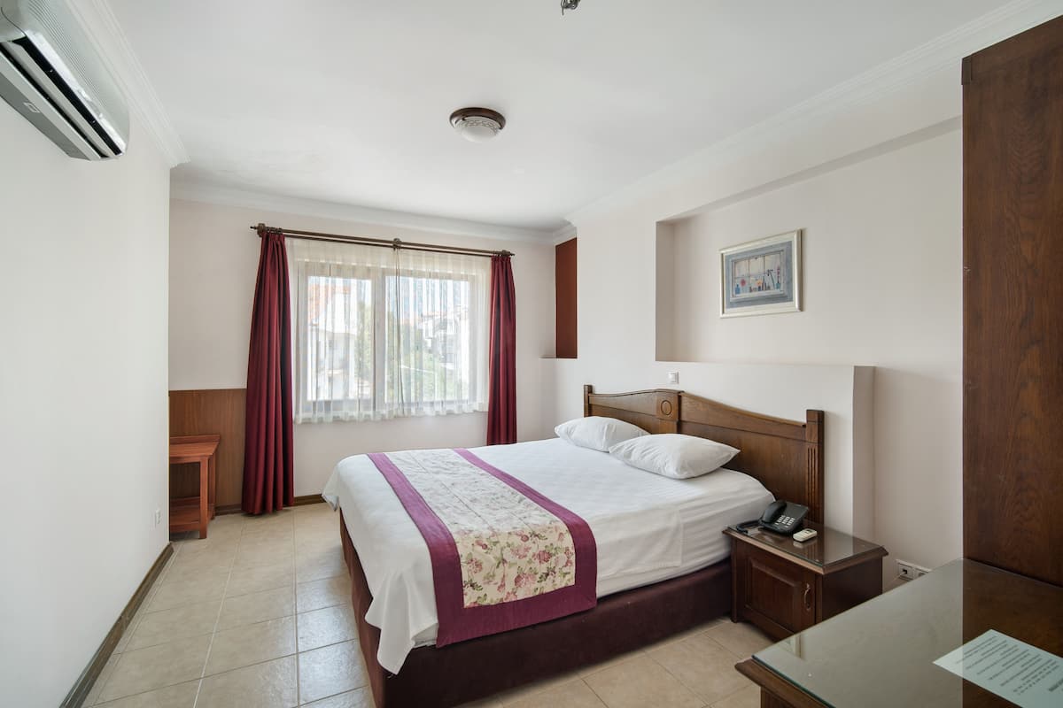 Une chambre d’hôtel avec un lit, une table de chevet, une commode et une fenêtre avec des rideaux.