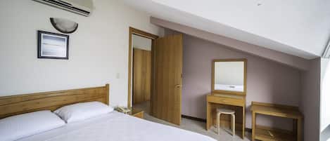 Quarto com cama, guarda-roupa de madeira, penteadeira com espelho e ar condicionado na parede.