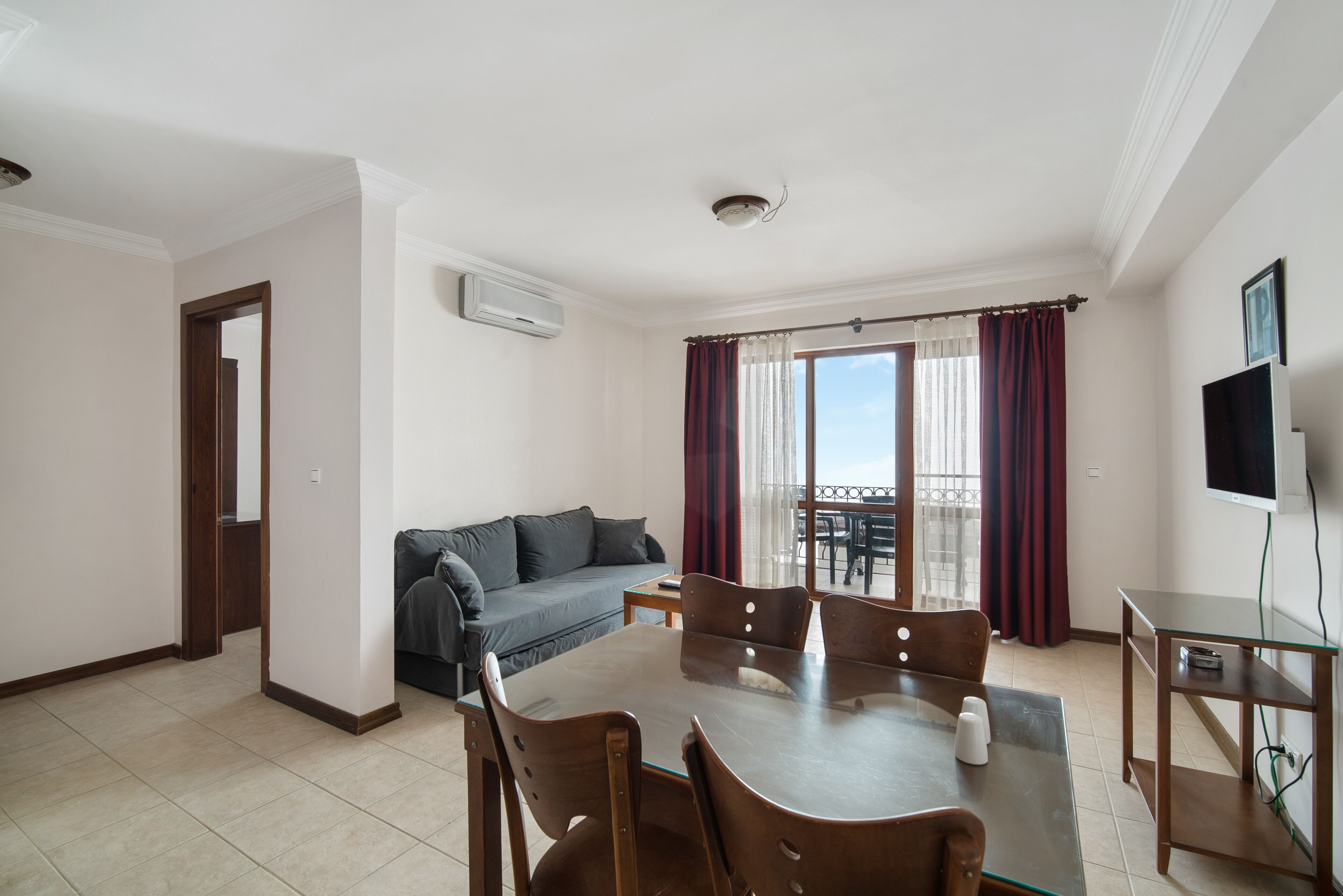 Una sala de estar moderna con una mesa de comedor, sillas, un sofá y un balcón con cortinas.