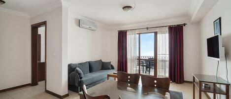 Una sala de estar moderna con una mesa de comedor, sillas, un sofá y un balcón con cortinas.