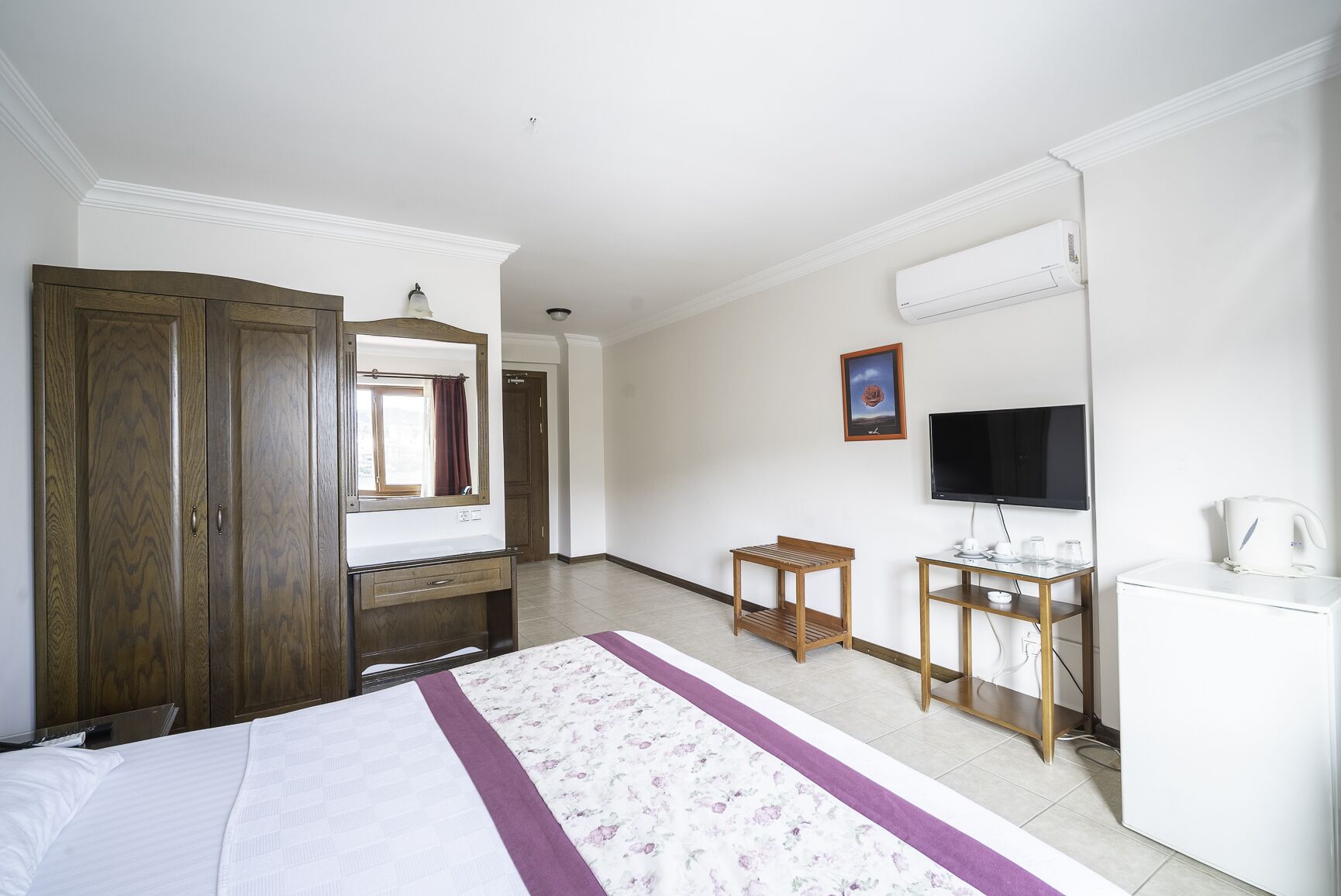 A hotel room with a bed, a desk, a television, a kettle, and a wardrobe.