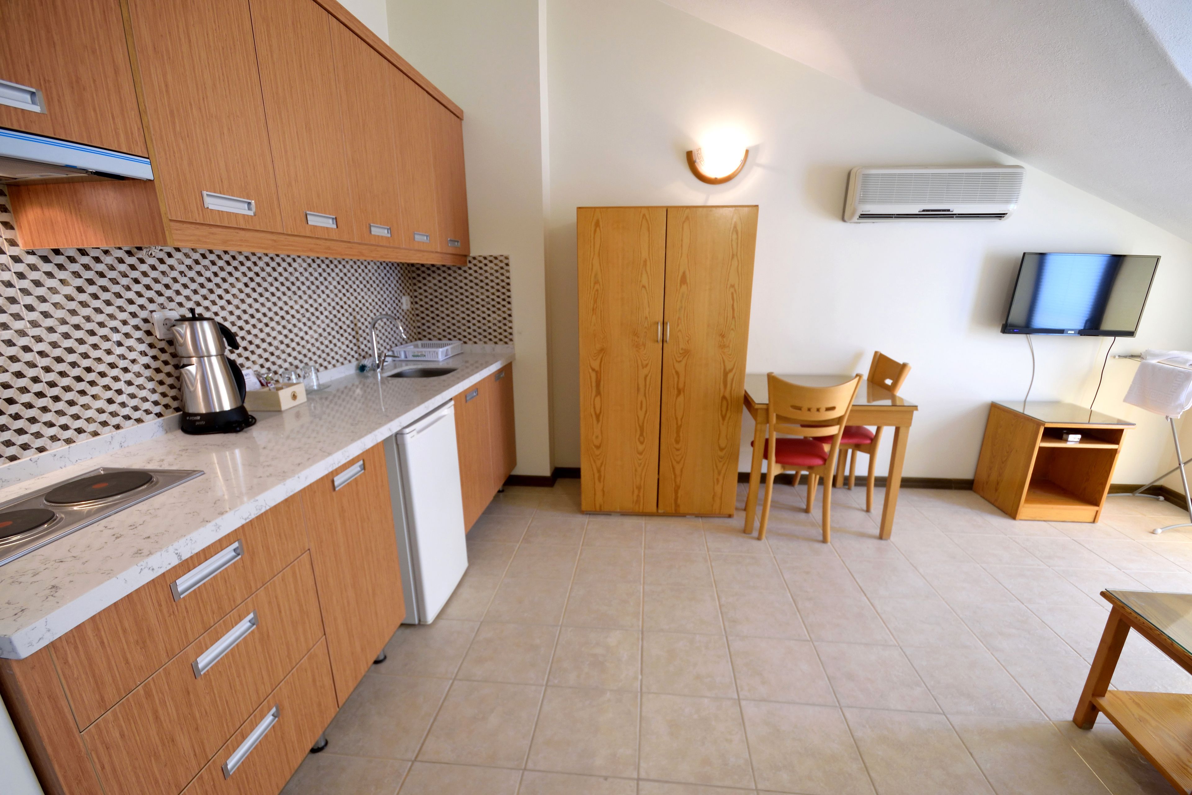 Una cocina compacta con armarios de madera, estufa integrada y un pequeño comedor con mesa y sillas.